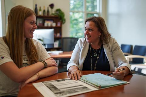 UNH employee sitting at a desk with a student reviewing paperwork